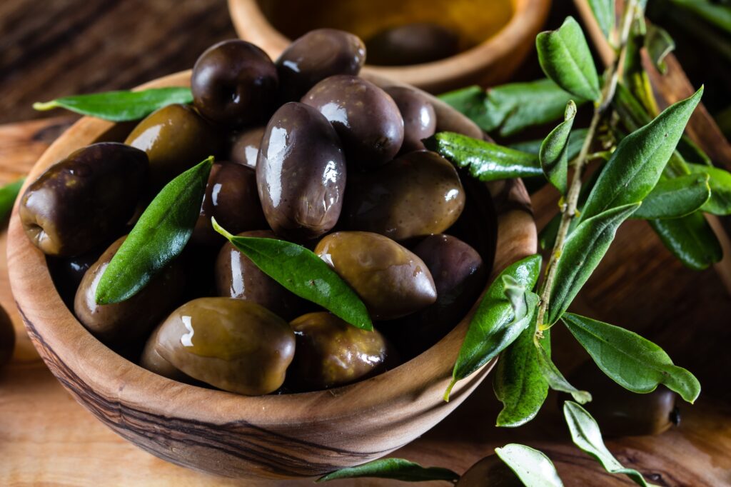 Olives and olive oil in olive wooden bowls, olive tree branch